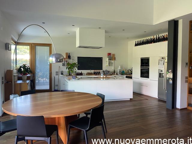 Open space con cucina ad isola zona living con tavolo rotondo in noce nazionale e sedie nere.